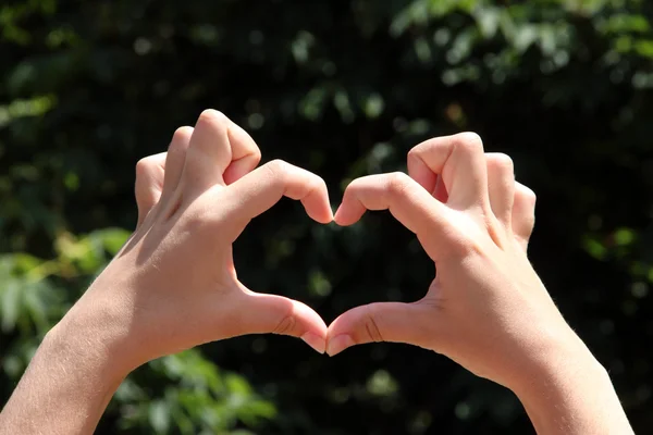 Fiatal lány, aki kezét a szív alakú kialakítása a természet háttér — Stock Fotó