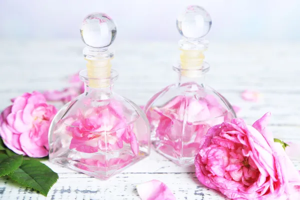 Óleo de rosa em garrafas na mesa de madeira colorida, no fundo claro — Fotografia de Stock