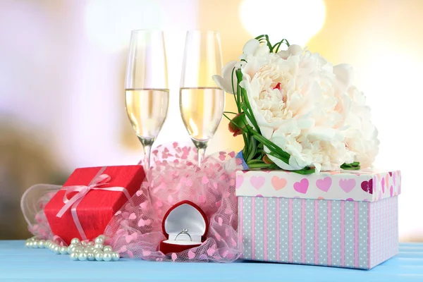 Beautiful wedding bouquet, gift box and wine glasses on  wooden table, on bright background — Stock Photo, Image