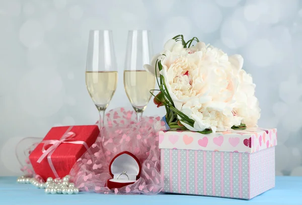 Beautiful wedding bouquet, gift box and wine glasses on  wooden table, on bright background — Stock Photo, Image