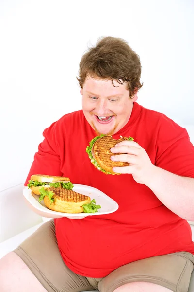 Fat man eating tasty sandwich on home interior background Stock Picture