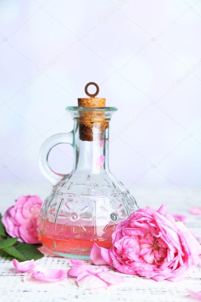 Rose oil in bottle on color wooden table, on light background