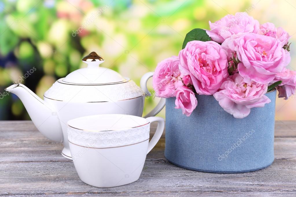 Breakfast tea with  teapot of fresh pink garden roses on wooden table, on bright background