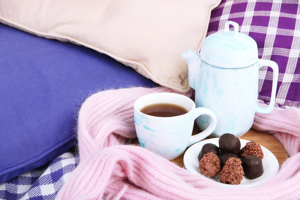 Cup and teapot with candies and scarf on wooden stand on bed close up — Stock Photo, Image