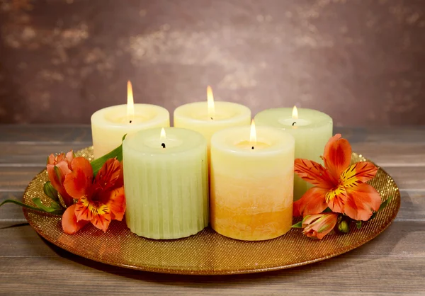 Mooie kaarsen met bloemen op tafel op bruine achtergrond — Stockfoto