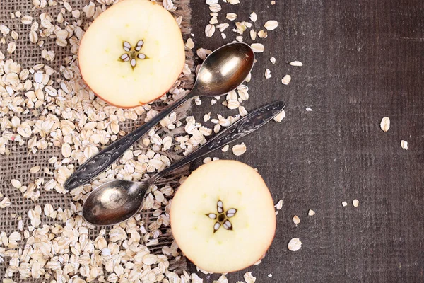 Apple with oatmeal and vintage spoons on sackcloth, on color wooden background — Stock Photo, Image