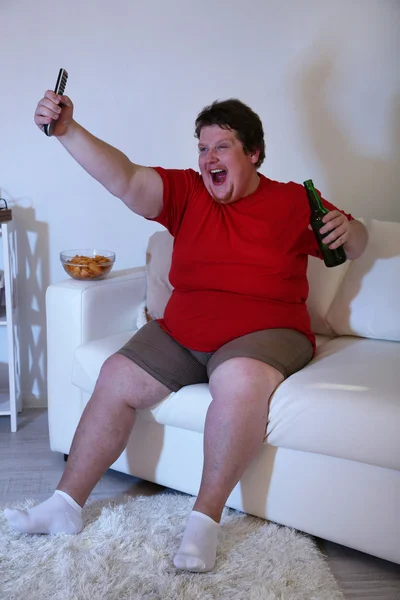 Lazy overweight male sitting on couch and watching television — Stock Photo, Image