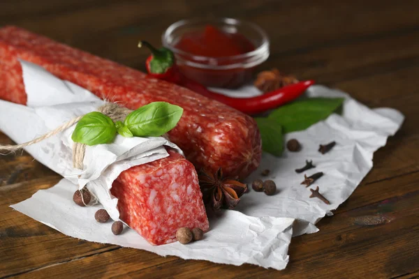 Tasty salami sausage and spices on wooden background — Stock Photo, Image