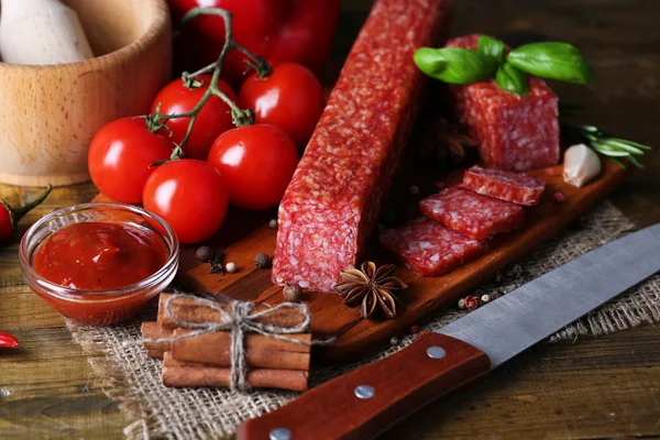 Tasty salami sausage and spices on wooden background — Stock Photo, Image