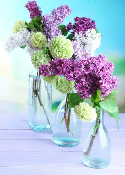 Bellissimi fiori primaverili in bottiglie di vetro, su tavolo di legno, su sfondo luminoso — Foto Stock