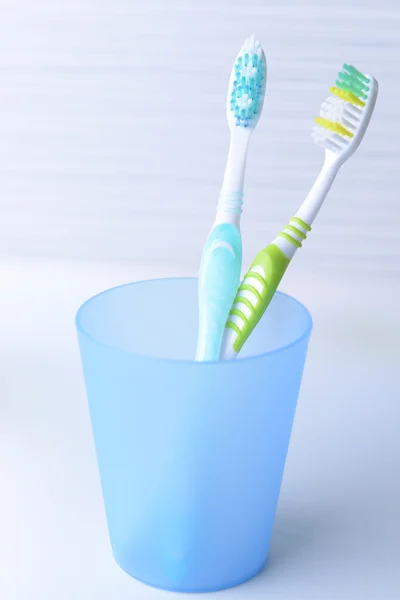 Cepillos de dientes en vidrio sobre mesa sobre fondo claro — Foto de Stock