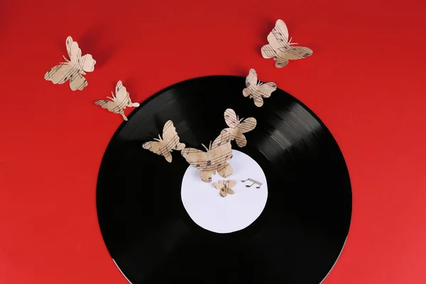 Ancien disque vinyle avec papillons en papier, sur fond rouge — Photo