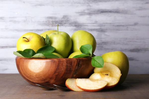 Rijp zoete appels met bladeren in schaal op houten ondergrond — Stockfoto