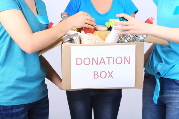 Volunteers with donation box with foodstuffs on grey background — Stock Photo, Image