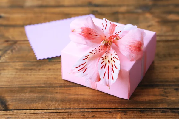 Presente rosa com arco e flor na mesa de madeira close-up — Fotografia de Stock
