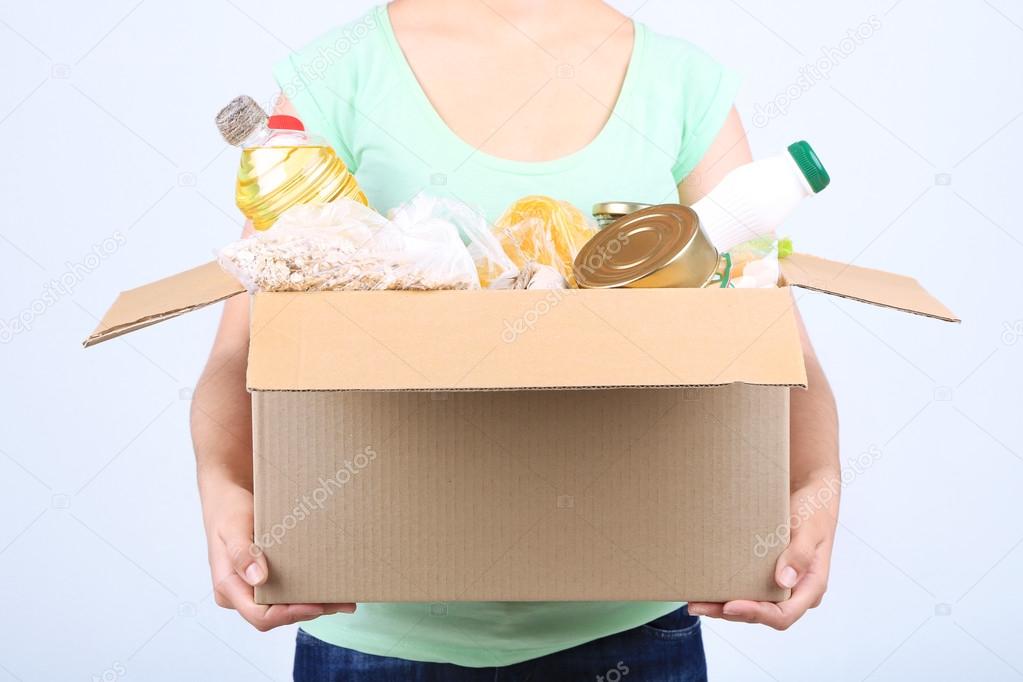 Volunteer with donation box with foodstuffs on grey background