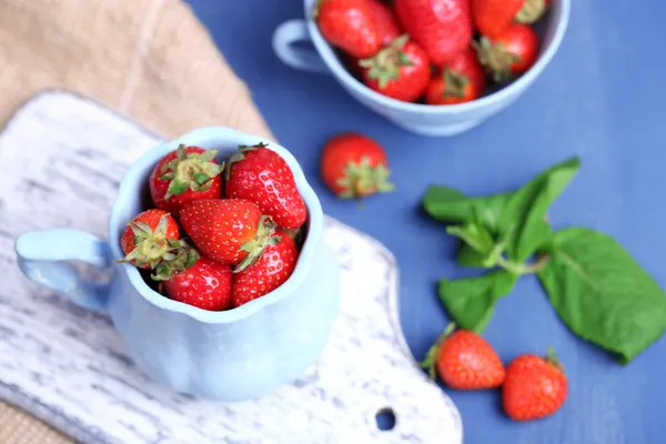 Reife süße Erdbeeren im Becher auf farbigem Holzhintergrund — Stockfoto