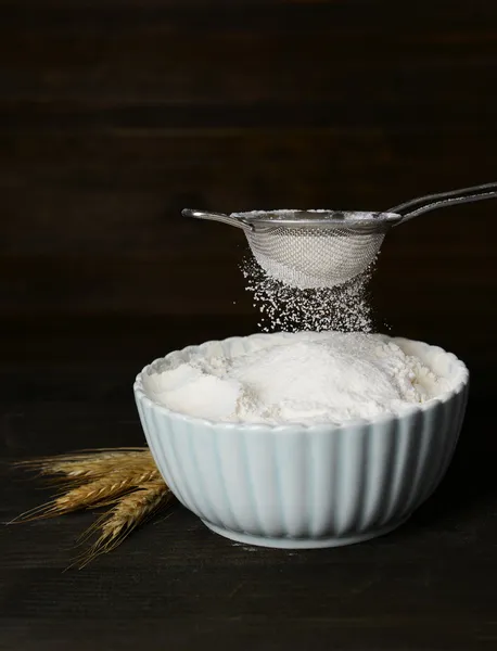 Sifting flour into bowl on table on wooden background — Stock Photo, Image