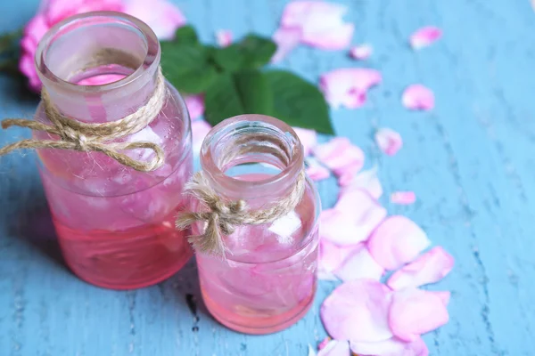 Aceite de rosa en botellas sobre fondo de madera de color — Foto de Stock