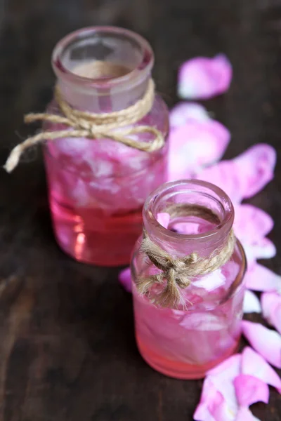 Aceite de rosa en botellas sobre fondo de madera de color — Foto de Stock