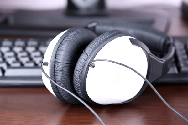 Headphone e teclado close-up em fundo de mesa de madeira — Fotografia de Stock