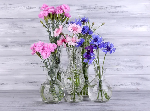 Krásné letní květiny ve vázách na šedém pozadí dřevěná — Stock fotografie