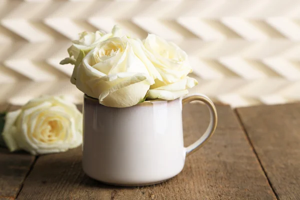 Schöne weiße Rosen in Tasse auf Holztisch — Stockfoto