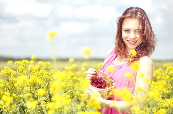 Beautiful young woman holding wicker basket with cherries in field — Stock Photo, Image