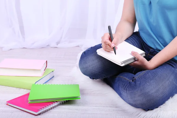 Closeup of young female student sitting on floor and studying, on light background — Stock Photo, Image