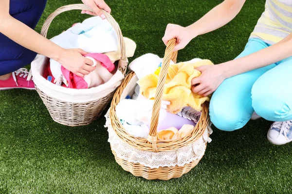 Vrouwen houden papiermanden met schone kleren, gras handdoeken en pinnen, op groen achtergrond — Stockfoto