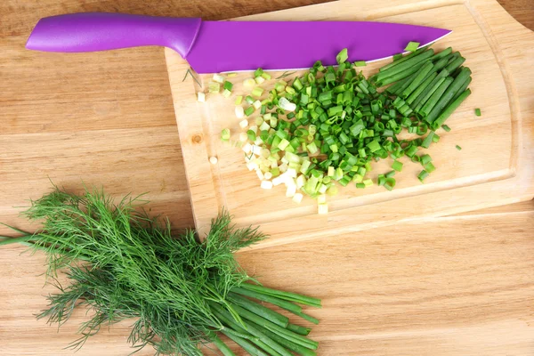 Chopped green onion with knife on cutting board on wooden table — Stock Photo, Image