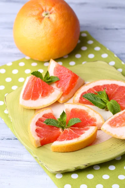 Reife Grapefruits auf Teller, auf Holztisch, auf hellem Hintergrund — Stockfoto