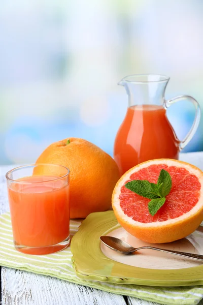 De helft van grapefruit, glas kruik met vers sap en lepel op plaat op lichte achtergrond — Stockfoto