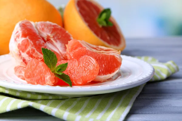 Ripe peeled grapefruits on plate, on color wooden table, on light background — Stock Photo, Image