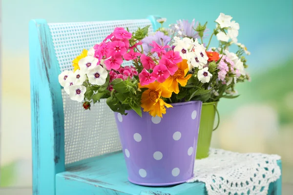 Bouquet of colorful flowers in decorative buckets, on chair, on bright background — Stock Photo, Image