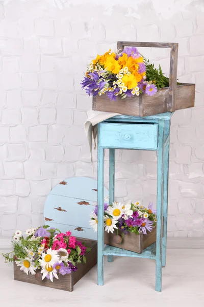 Hermosas flores en cajas en soporte de madera sobre fondo claro — Foto de Stock