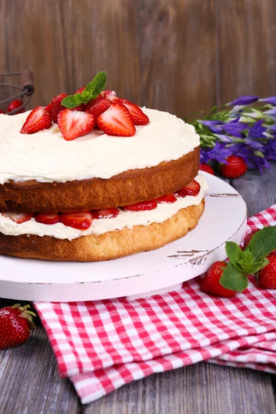 Delicious biscuit cake with strawberries on table on wooden background — Stock Photo, Image