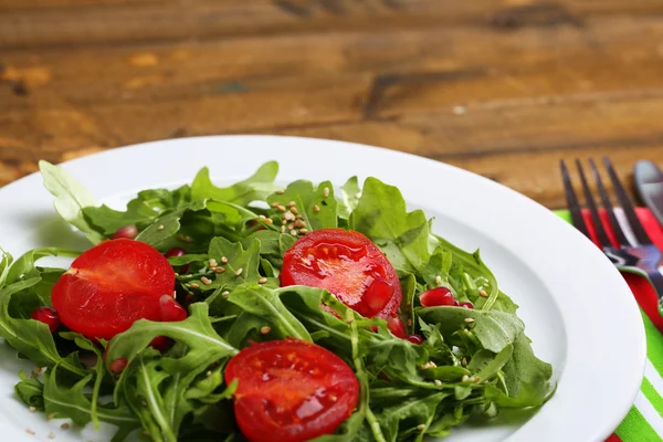Grön sallad med rucola, tomater och sesam på plattan, på trä bakgrund — Stockfoto