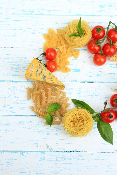 Different pasta, cheese and tomatoes on wooden table close-up — Stock Photo, Image