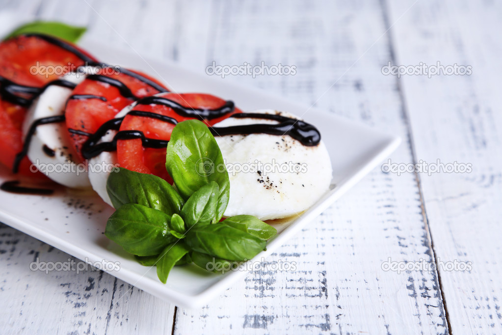 Caprese salad with mozarella cheese, tomatoes and basil on plate, on wooden table background