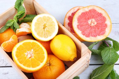 Fresh citrus fruits with green leaves in wooden box on color wooden background clipart