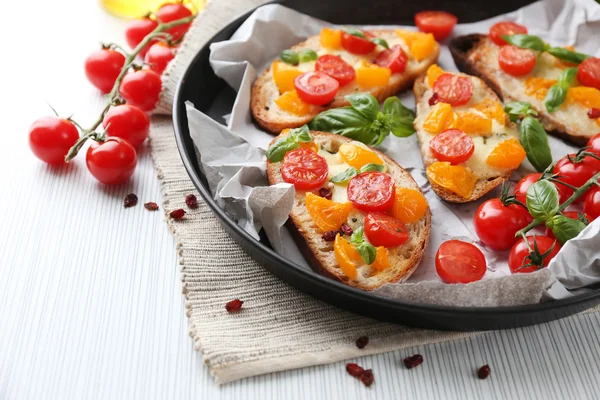 Tasty bruschetta with tomatoes in pan, on table — Stock Photo, Image