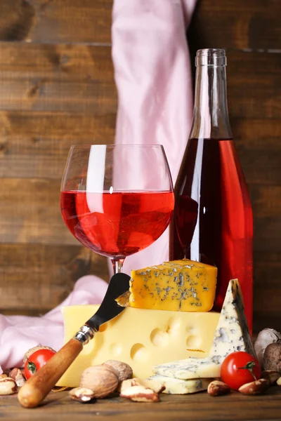 Roze wijn en verschillende soorten kaas op houten achtergrond — Stockfoto