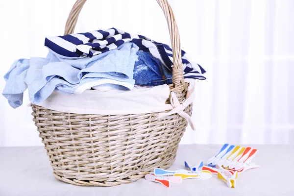 Colorful clothes in basket and pins on table, on light background — Stock Photo, Image