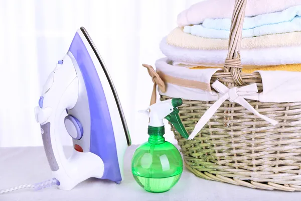 Colorful towels in basket, iron on light background — Stock Photo, Image