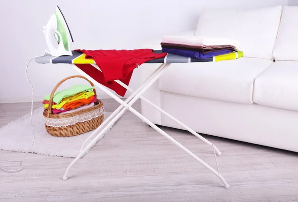 Basket with laundry and ironing board on light background — Stock Photo, Image