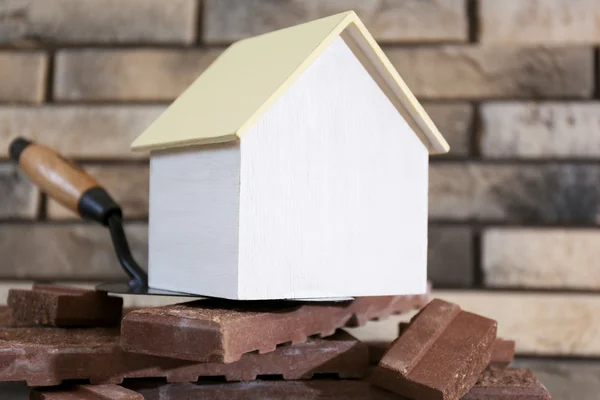 Casa giocattolo in legno su spatola e piastrelle su sfondo muro di mattoni — Foto Stock