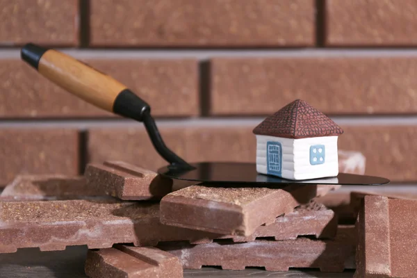 Wooden toy house on trowel and tiles on brick wall background — Stock Photo, Image