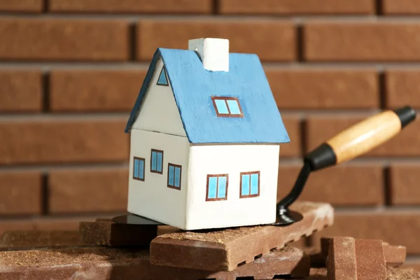 Wooden toy house on trowel and tiles on brick wall background — Stock Photo, Image