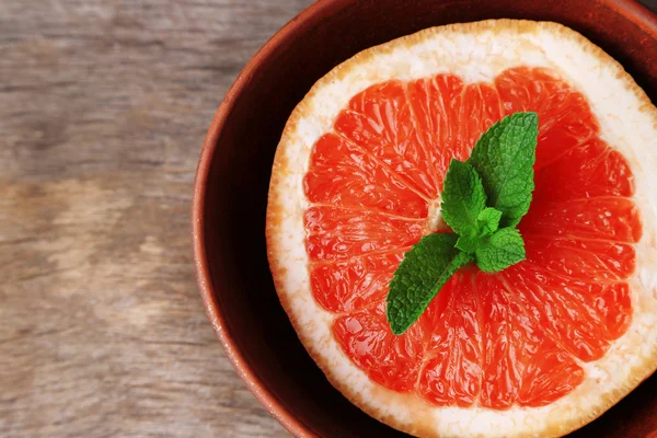 Deel van rijp grapefruit in kom, op houten achtergrond — Stockfoto